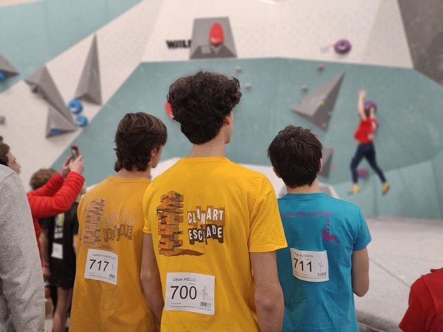 Trois jeunes grimpeurs Clamart Escalade en t-shirts jaunes (dossards 717, 700, 711) regardant la compétition régionale de bloc à Aubervilliers, janvier 2023